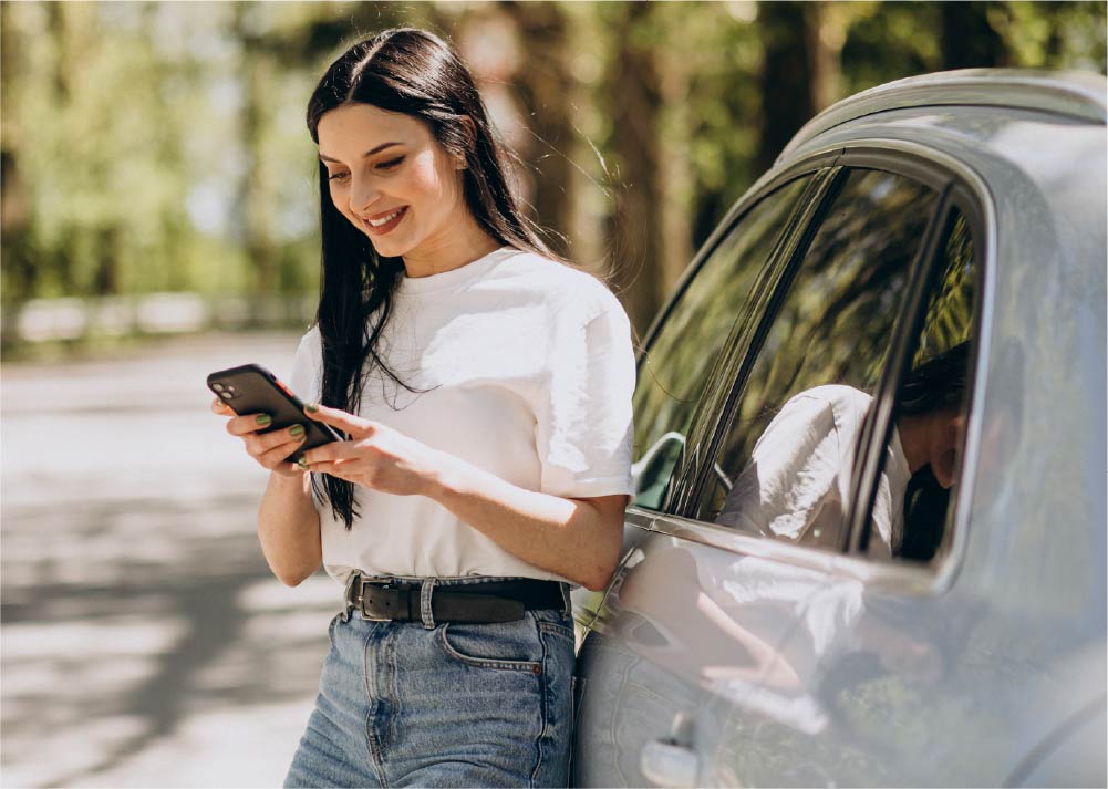 Smiling woman leaning against white car using smart phone